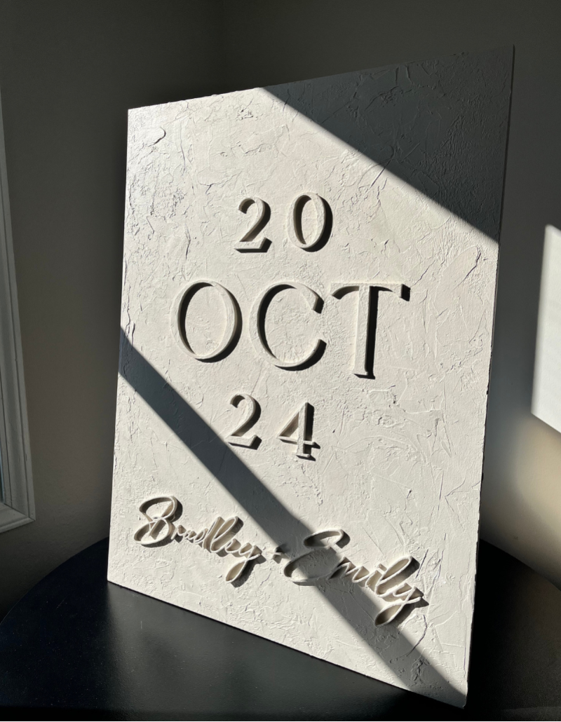 White textured card with '20 OCT 24' and 'Brendley & Emily' embossed on it, against a dark background.
