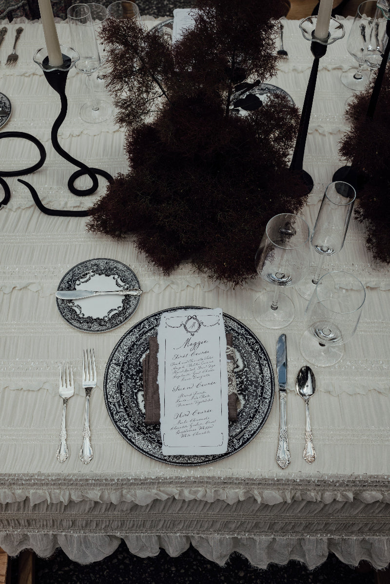 Elegant table setting with black and white plates, a custom menu, silverware, and decorative elements.